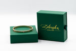 Gold bracelet on a green Zelenska Jewellery box against a white background